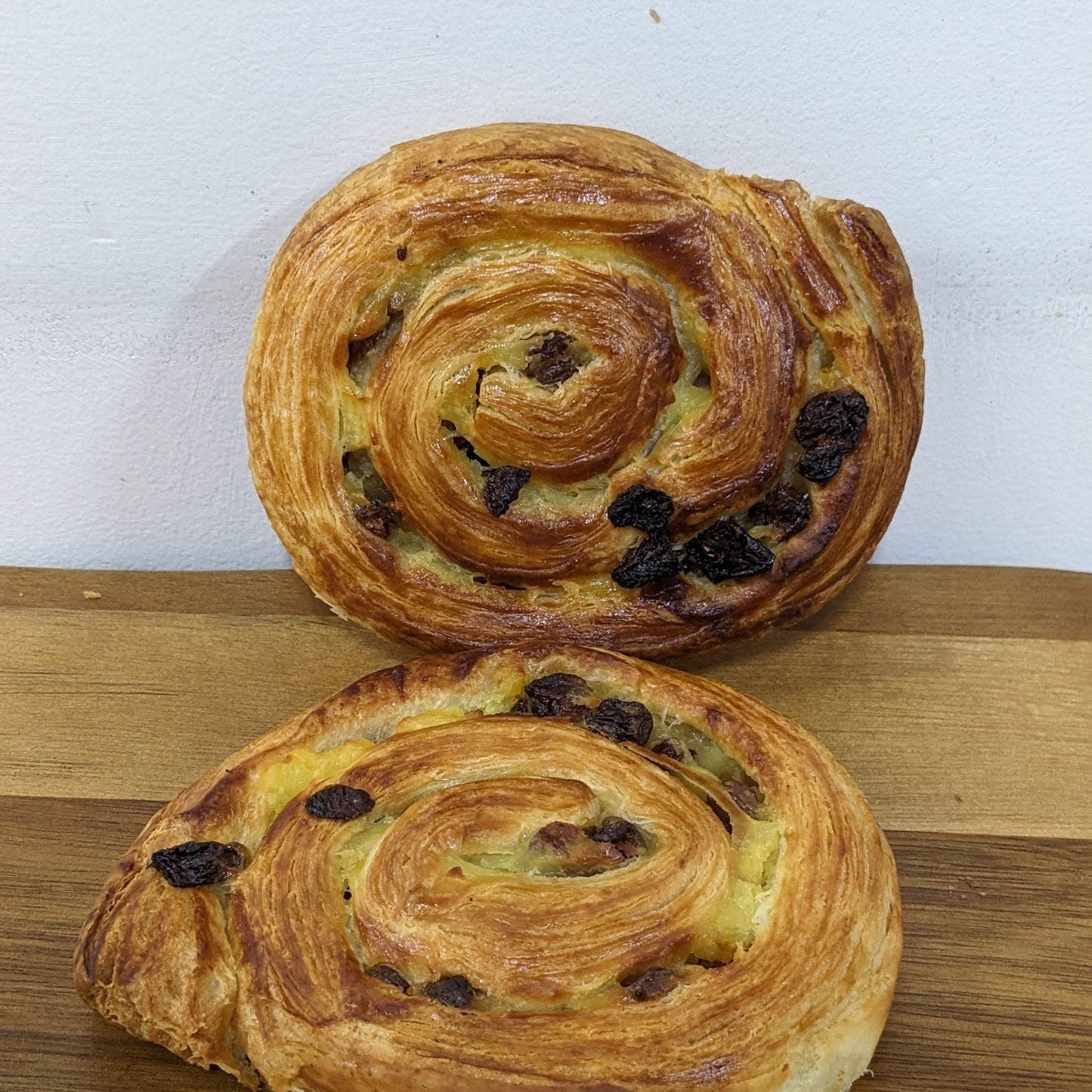Two freshly baked Easter escargot pastries with visible raisins, placed on a wooden surface.